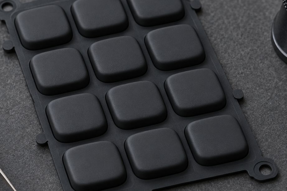 Detail: moulded black silicone keypad with raised legends on a workbench.